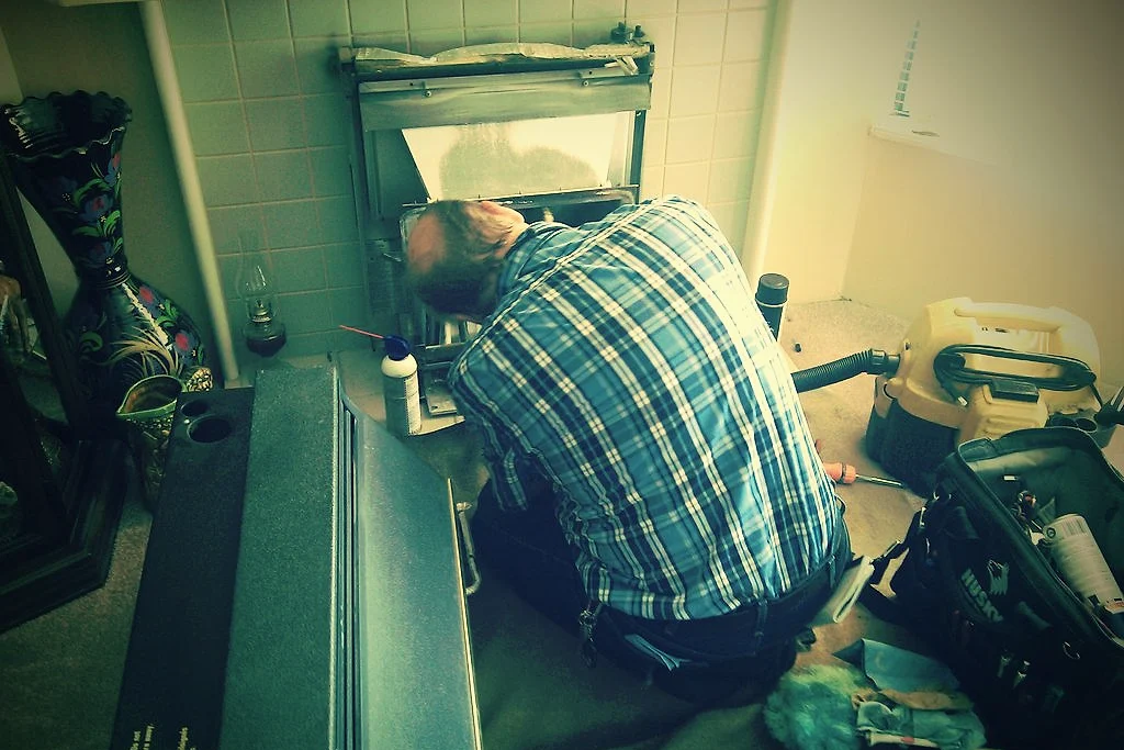 A plumber kneeling under a sink to fix a leak