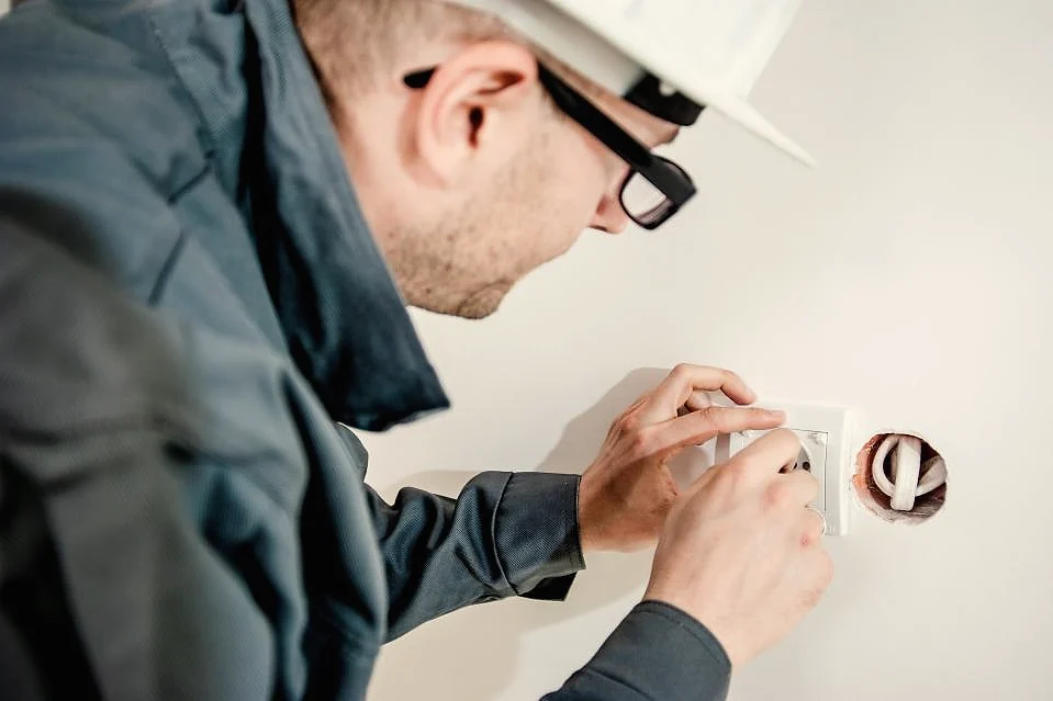 A technician in a hard hat repairing an outlet