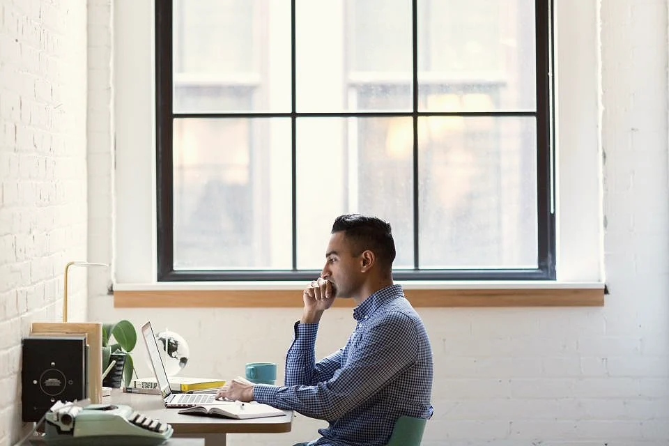 A manager on a phone call at his desk beside a tall window