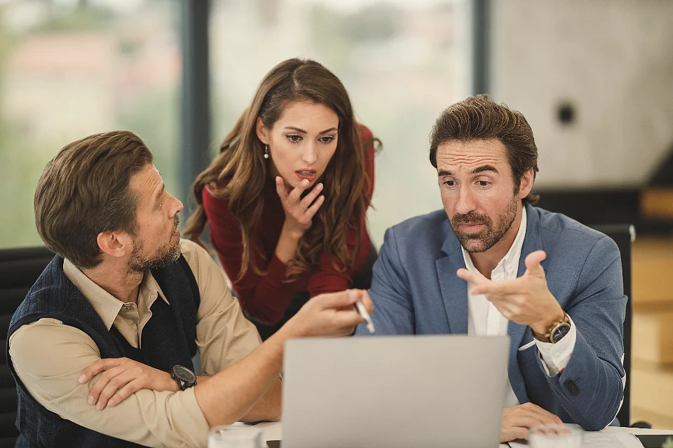 Three colleagues discussing numbers around a laptop