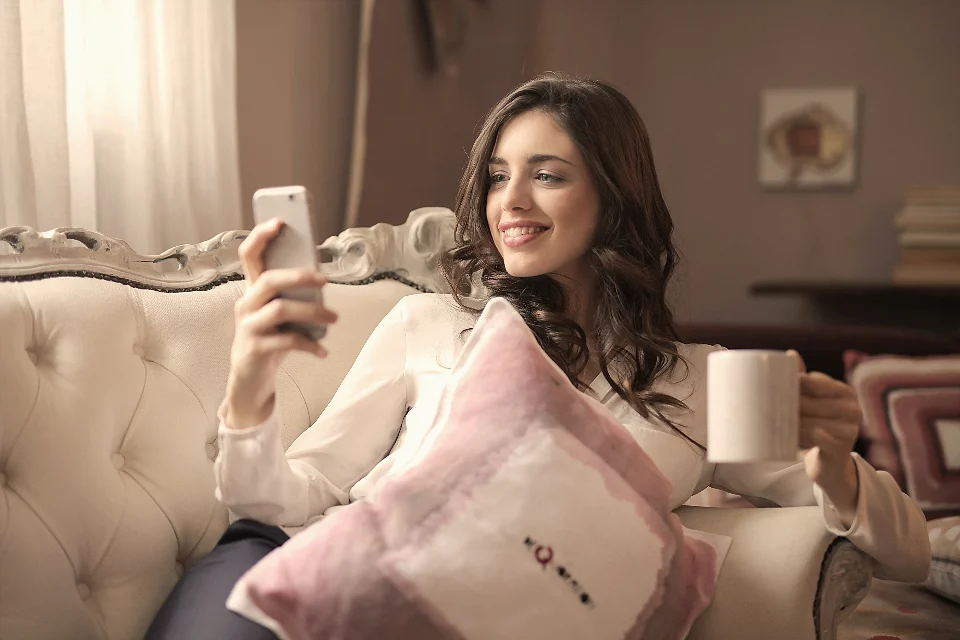 A young woman on a cream sofa smiling at her phone